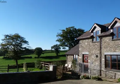 a large stone house with a field in the background at Beudy Bach in Lampeter