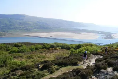 a group of people walking on a hill overlooking a body of water at Beudy Taicroesion in Barmouth