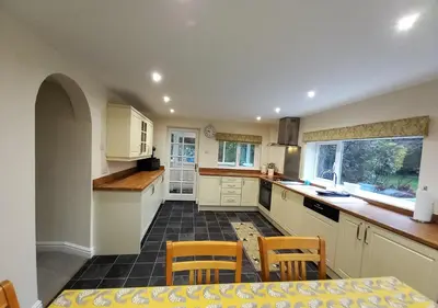 a kitchen with white cabinets and a table and chairs at Gerddi'r Coed in Dolgellau