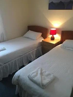 two beds in a room with a lamp on a night stand at Four Seasons Budget in Aberystwyth