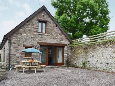 a stone cottage with a picnic table and an umbrella at Llaethdy-Milkhouse in Talgarth
