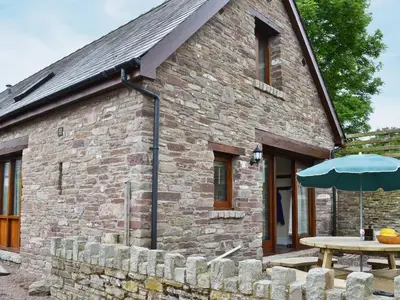 a stone building with a table and an umbrella at Llaethdy-Milkhouse in Talgarth