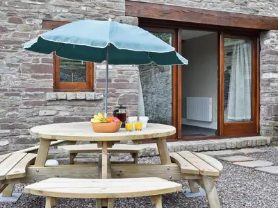 a picnic table with a blue umbrella and benches at Llaethdy-Milkhouse in Talgarth