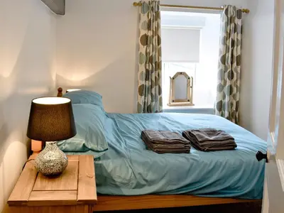 a bed with blue sheets and a table with a lamp at Pendref in Trawsfynydd