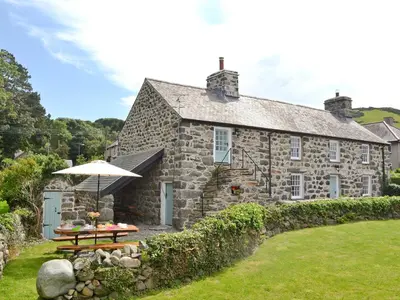 an old stone house with a picnic table and an umbrella at Ty Newydd in Llwyngwril