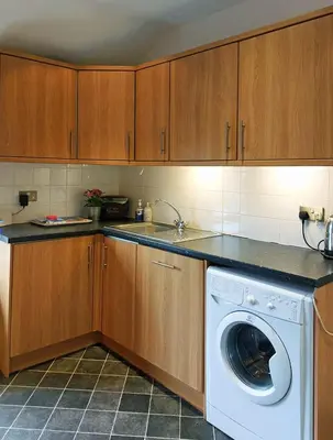 a kitchen with a washing machine and wooden cabinets at Salt Marsh Apartment in Tywyn