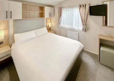 a large white bed in a small room with a window at Pencnwc Holiday Park in Llanllwchaiarn