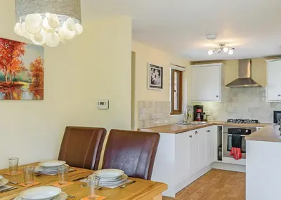 a kitchen with a wooden table and chairs and a kitchen with white cabinets at Slate House Lodges in Towyn