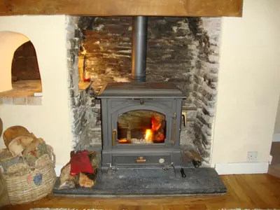 a wood stove in a room with a stone wall at Ceiros Cottage in Llangammarch Wells