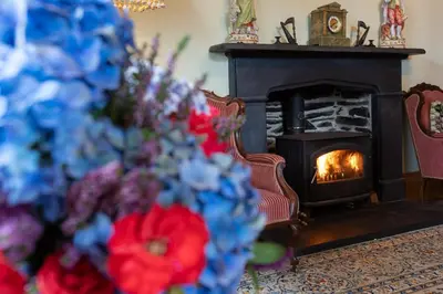 a fireplace in a living room with flowers in front of it at Taldraeth - Old Vicarage Guest House in Penrhyndeudreath