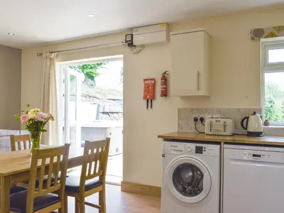 a kitchen with a washing machine and a table with chairs at Brynllin Holiday Cottages - Dildre in Penuwch