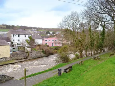 a river with two benches next to a river with buildings at Y Bwthyn Pren in Aberaeron