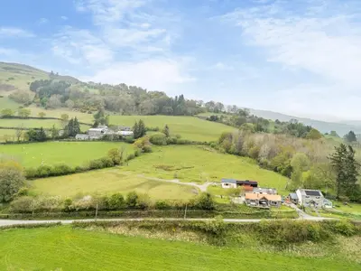 a green hill with houses and a road on it at Wern Ddu Cottage in Pen-y-bont-fawr