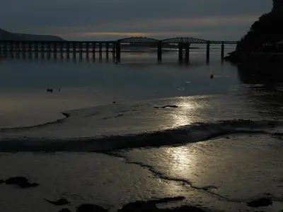 a bridge over a body of water with a pier at Seascape in Barmouth