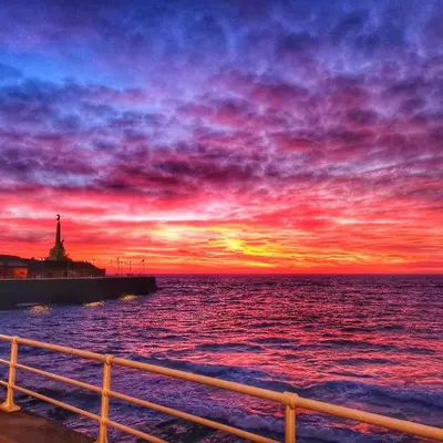 a sunset over the ocean with a lighthouse at Sea retreat caravans in Aberystwyth