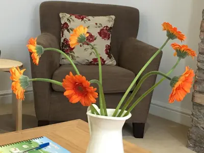 a vase with orange flowers on a table in front of a chair at March Cottage Brecon in Brecon