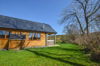 a log cabin with a grassy yard next to a house at LLanddewi Retreat in Llanddewi Ystradenny