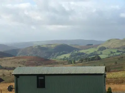 a green building in a field with mountains in the background at Upper Gilwern Quarry Hut in Llandrindod Wells