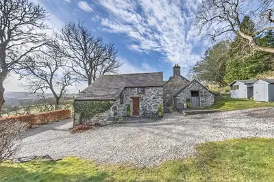 an old stone house on a gravel driveway at Beautiful 16th Century Ty Cerrig Cottage, set in stunning grounds with great views in Corwen