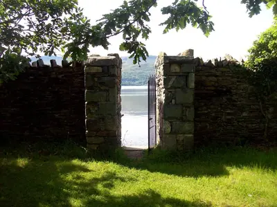 an open gate in a stone wall with a body of water at Yr Hen Feudy in Barmouth