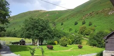 a green hillside with a house and a grass field at Lake Cottages at Cwm Chwefru in Llanafan-fawr