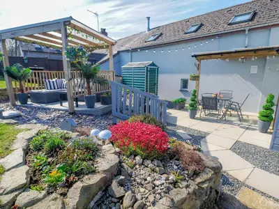 a patio with a garden with flowers and a house at Y Bwthyn in Tal-gareg