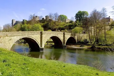 a stone bridge over a river with a castle in the background at The Oaks in Church Stretton