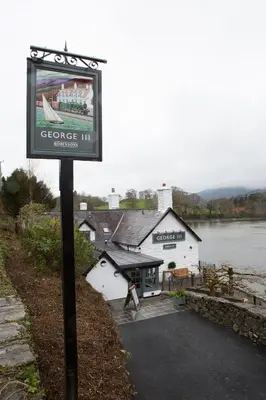 a sign in front of a building next to a river at George III Hotel in Penmaenpool