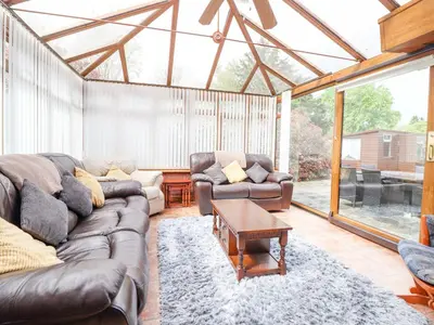 a living room with a couch and chairs in a conservatory at 1 The Beeches in Llangollen