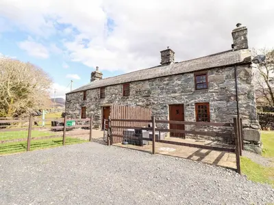 an old stone building with a fence and a bench at Cwm Yr Afon Cottage in Harlech