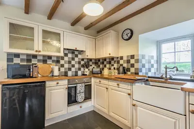 a kitchen with white cabinets and a clock on the wall at Ty Capel Jeriwsalem in Trawsfynydd