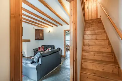 a living room with a black leather couch and stairs at Ty Capel Jeriwsalem in Trawsfynydd