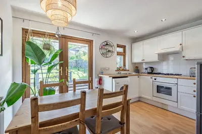 a kitchen with white cabinets and a wooden table and chairs at Gorwel in Blaenau-Ffestiniog