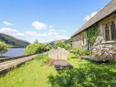 an old stone building next to a body of water at St Mary's in Tal-y-llyn
