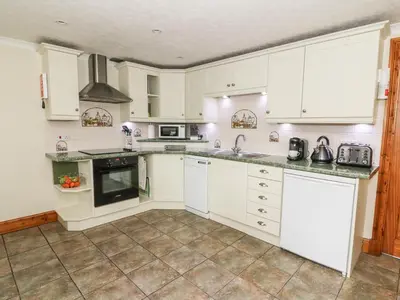 a white kitchen with white cabinets and appliances at Tangaer Cottage in Cellan