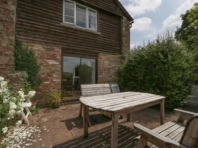 a wooden table and benches in front of a house at Wheelbarrow Cottage in Stoke Prior