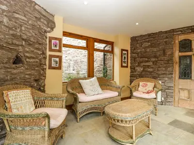 a living room with wicker chairs and a stone wall at Wheelbarrow Castle in Stoke Prior