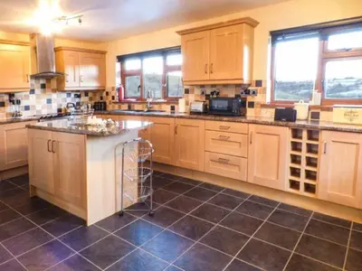 a large kitchen with wooden cabinets and a tile floor at Tynddol Bungalow in Llanbadarn-fynydd