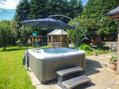 a hot tub with an umbrella in a yard at Tynddol Bungalow in Llanbadarn-fynydd