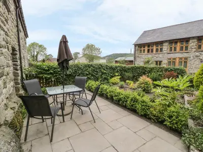 a patio with a table and chairs and a garden at Hendoll Cottage 1 in Fairbourne
