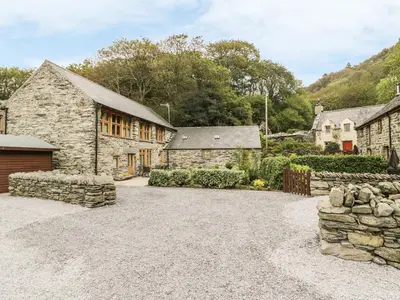 an exterior view of a stone house with a driveway at Hendoll Barn in Fairbourne