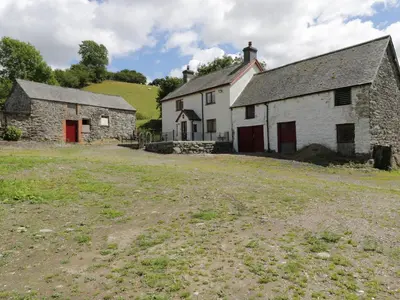 an old stone building with a red door in a field at Maerdy Cottage in Bettws Gwerfil Goch