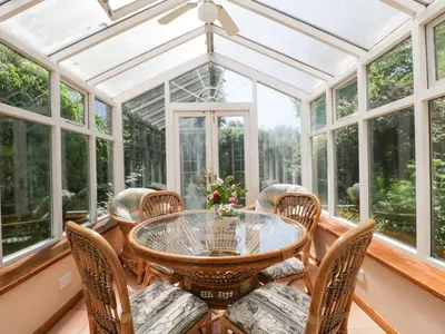 a conservatory with a glass table and chairs at Lower Court Byre in Kinsham