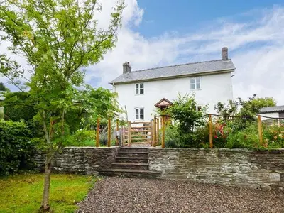 a white house with a stone wall and a tree at Gatehouse in Painscastle