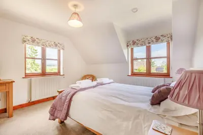 a bedroom with a large bed and two windows at Byne Brook Cottage in Wistanstow