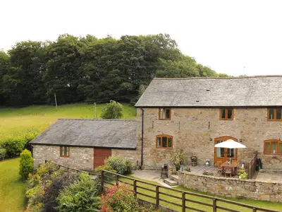 an old stone house with a table and an umbrella at Little Cow House in Chirk