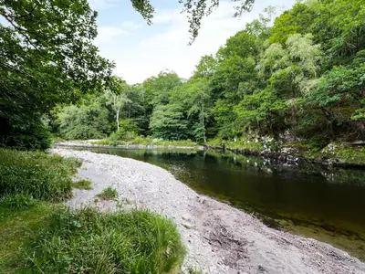 a river with trees and a rocky shoreline at Hen Gelligemlyn - The Annexe in Llanfachreth