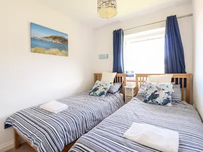 two beds in a bedroom with blue curtains at Sealyons in Fairbourne