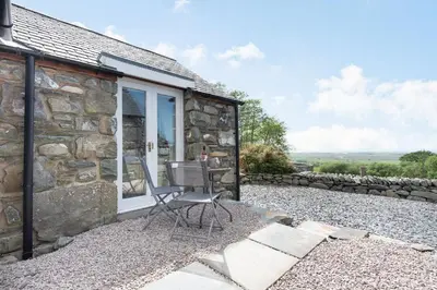 a stone cottage with a chair in front of it at Y Becws in Llanbedr