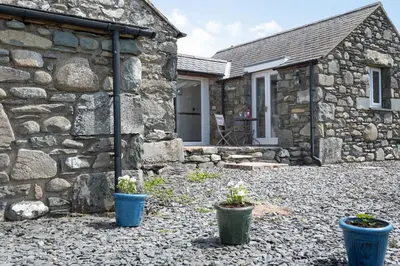 a stone house with two potted plants in front of it at Y Becws in Llanbedr